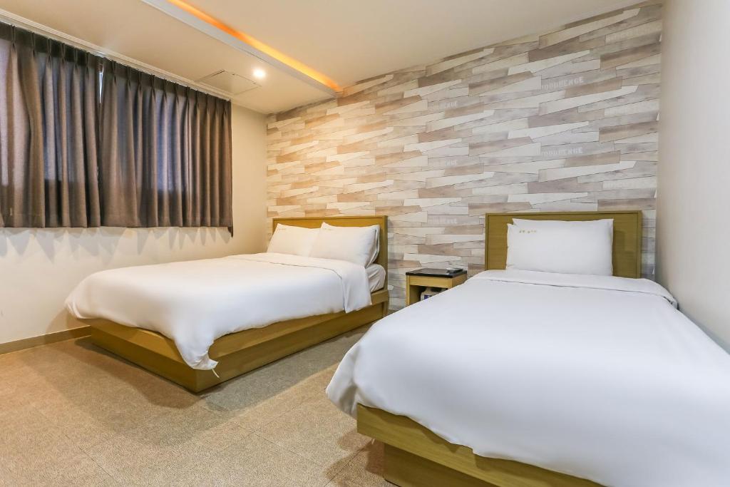 a bedroom with two beds and a stone wall at Aliba Hotel in Jeju
