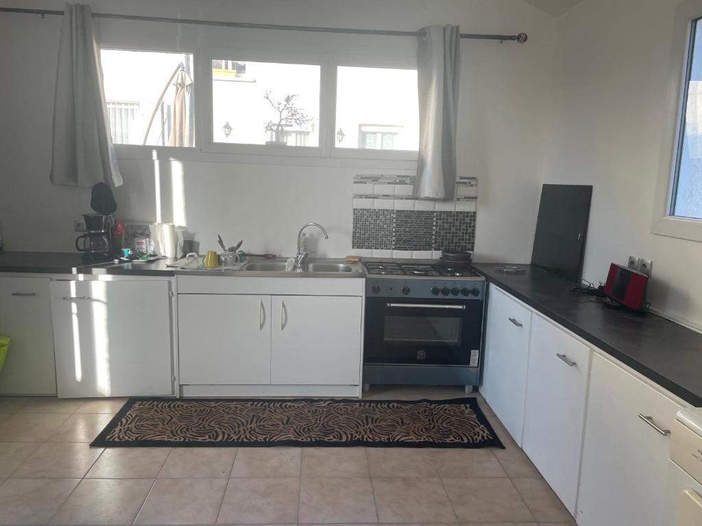una cucina con armadietti bianchi, piano cottura e finestra di Maison T 1 meublé confort proche aéroport a Pusignan