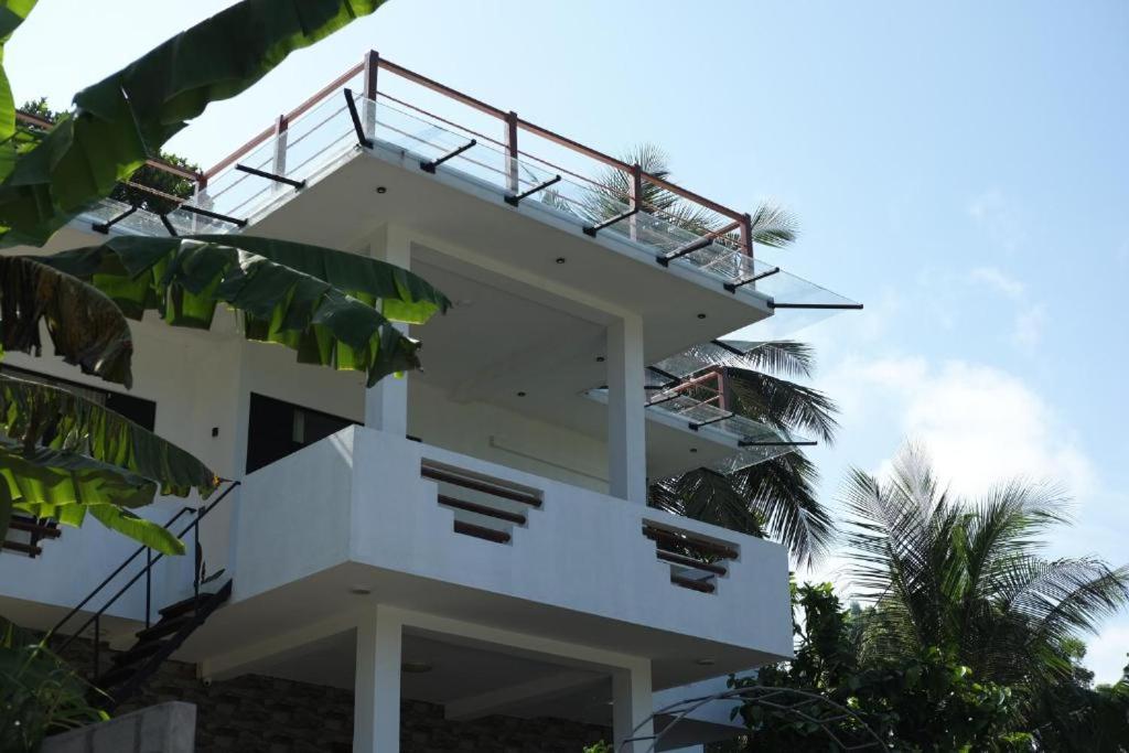 a white building with a balcony and some palm trees at Divya Sea View in Dodampahala East