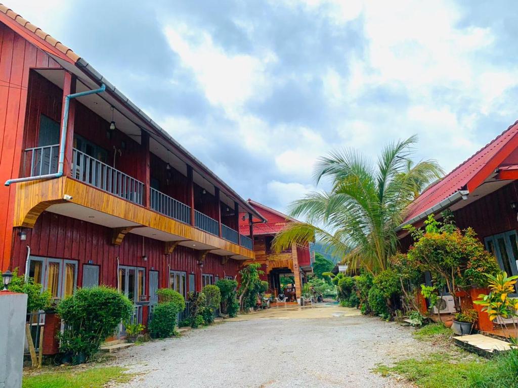 萬榮的住宿－Inthila Garden Guest House，两座红色建筑之间一条土路,两座建筑的棕榈树