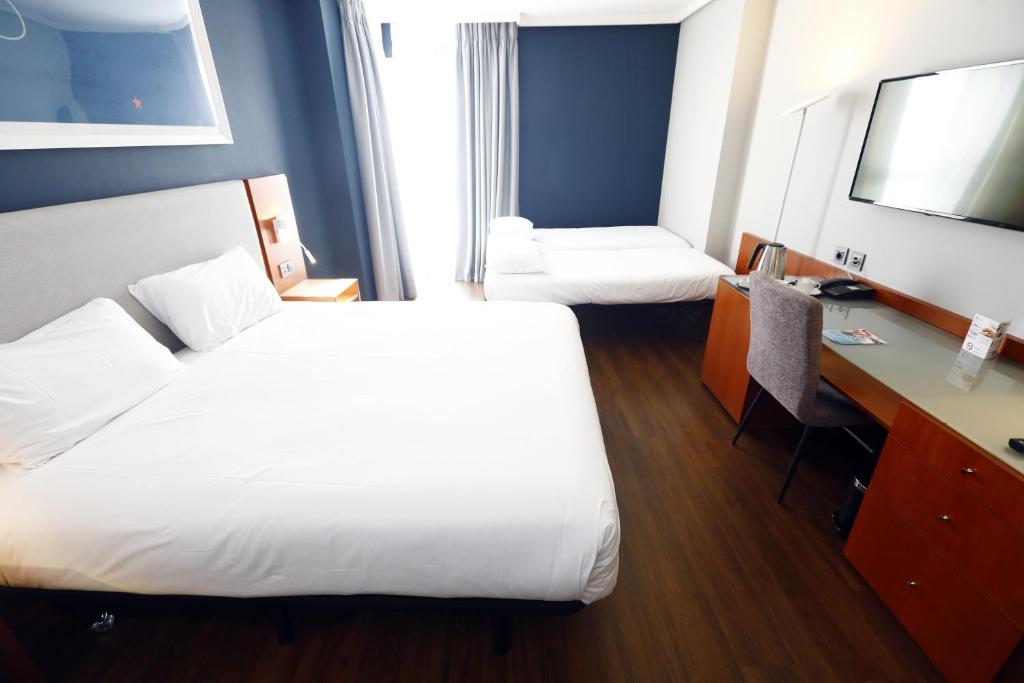 a hotel room with two beds and a desk at Travelodge Madrid Coslada Aeropuerto in Coslada