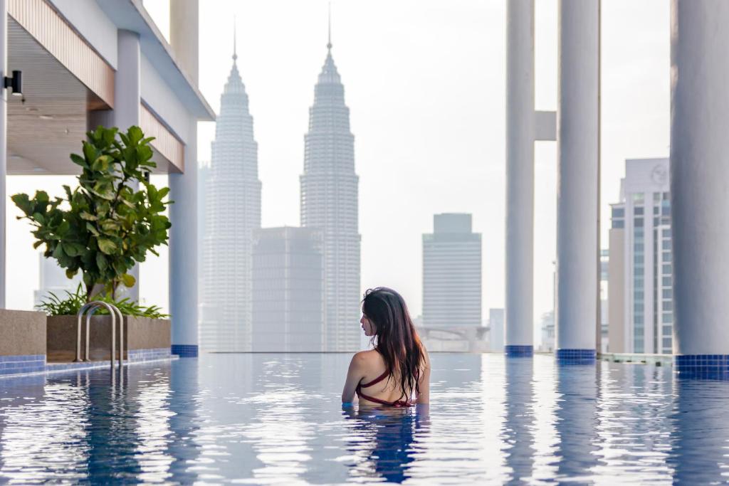 The Colony & The Luxe, Kuala Lumpur by Canopy Lives في كوالالمبور: امرأة تجلس في مسبح لا نهاية له في مدينة