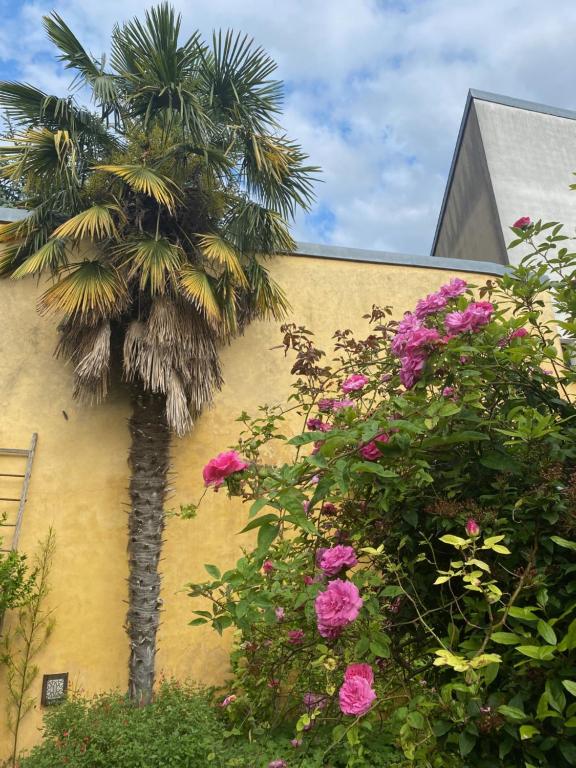 a palm tree next to a yellow building with flowers at Maison piscine centre historique de Romainville in Romainville