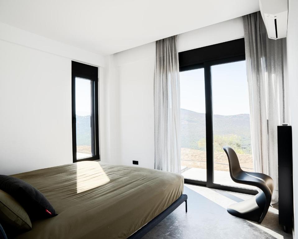 a bedroom with a bed and a chair and windows at KATHOS RESIDENCE in Kavoúsion