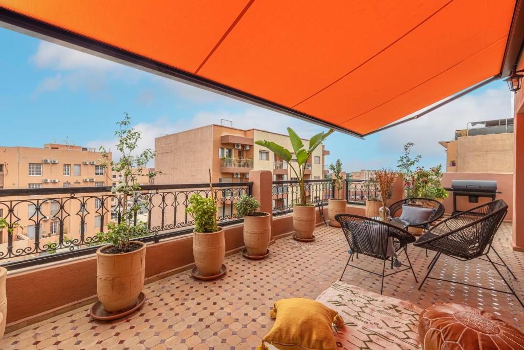 a balcony with chairs and potted plants and an orange umbrella at L'Atlas - Appartement Authentique à Gueliz in Marrakesh