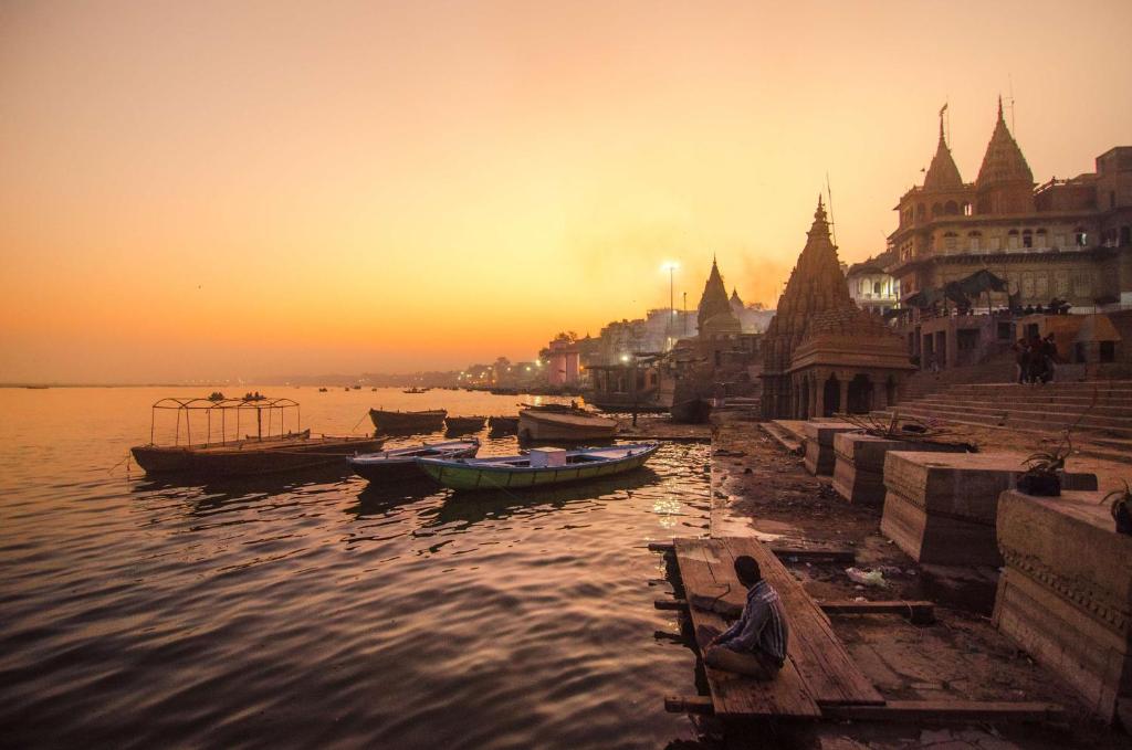 a person sitting on a dock in the water with boats at Radisson Hotel Varanasi in Varanasi