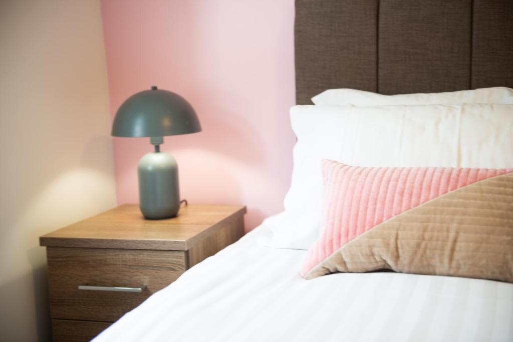 a lamp on a night stand next to a bed at The 'Pinky' - Beautiful 1 Bed Apartment in Hatfield - FREE Parking - Near Uni & Business Park - Long stays - Corporate, Leisure, Contractors in Hatfield