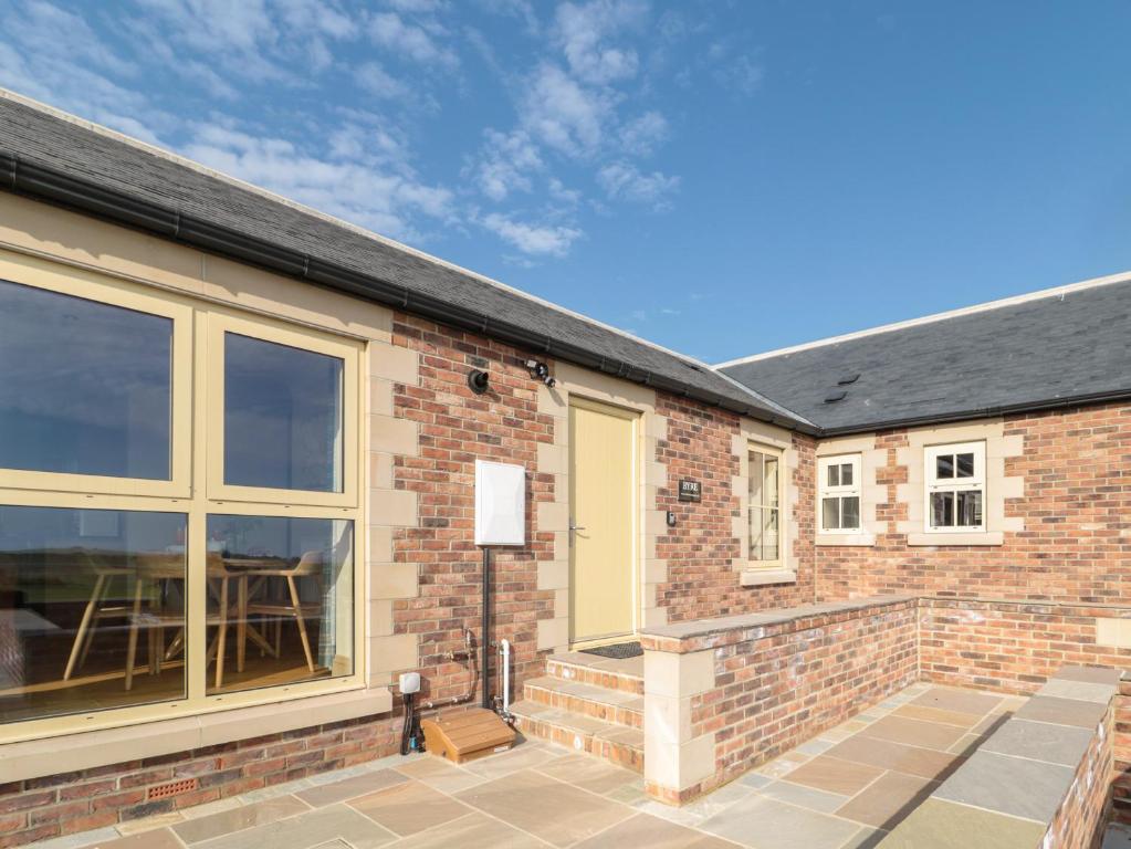 a brick house with a large window and a patio at Byre Cottage in Alnwick