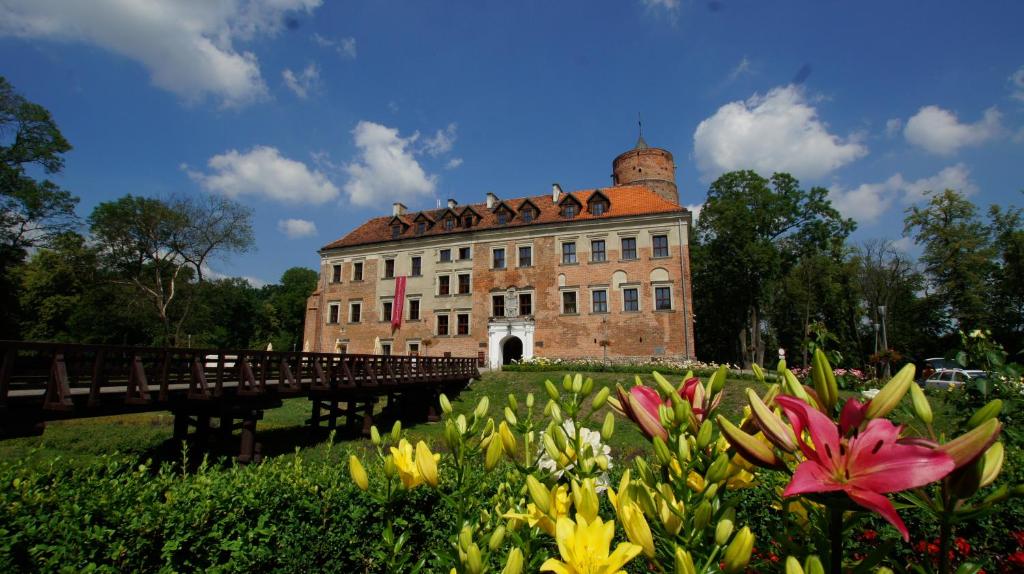 un edificio con un puente y flores delante de él en Zamek Uniejów, en Uniejów