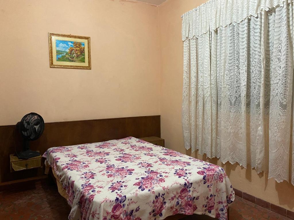 a bedroom with a bed with a floral bedspread and a window at Casa da vovó Marta in Itanhaém