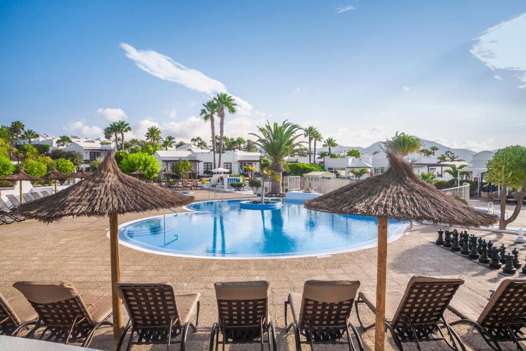 a pool with chairs and umbrellas on a beach at Jardines del Sol in Playa Blanca