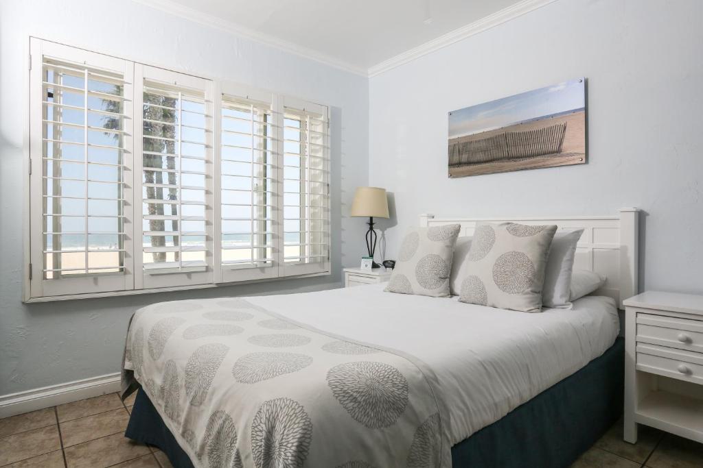 a bedroom with a white bed with white pillows and windows at Venice on the Beach Hotel in Los Angeles