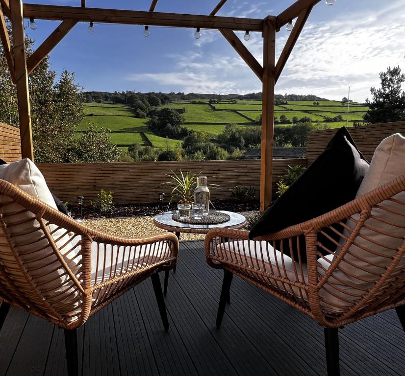 two wicker chairs and a table on a patio with a view at Holmfirth Hideaway in Holmfirth