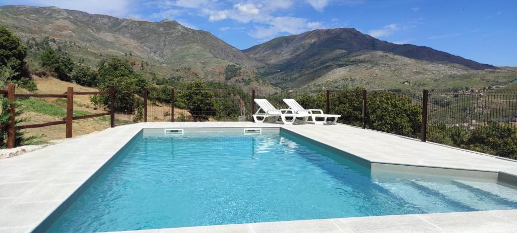 a swimming pool with two white chairs and mountains at Quinta do Torgal - Alojamento Local in Unhais da Serra