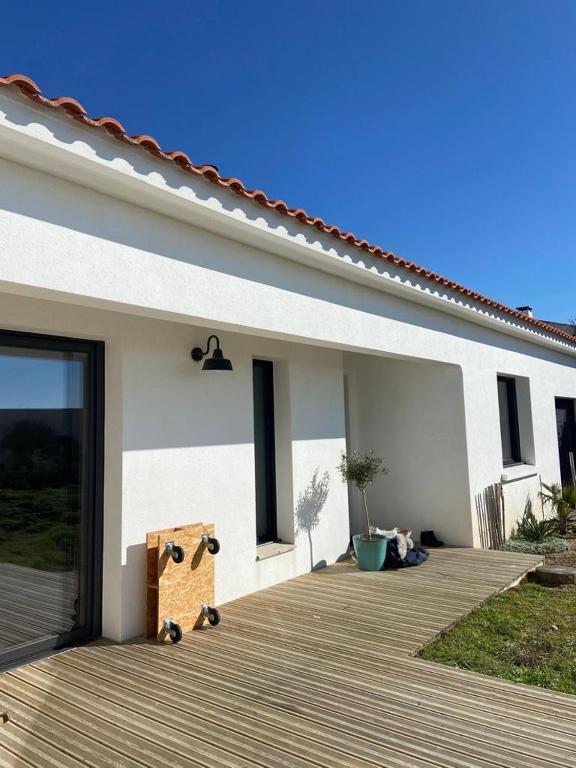 a white house with a wooden porch with a deck at Jolie villa face aux dunes et mer in Brétignolles-sur-Mer
