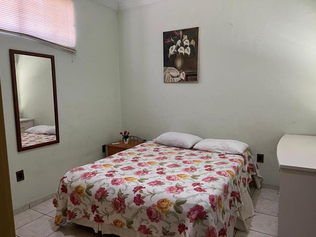 a bedroom with a bed with a floral bedspread and a mirror at Casa 3 suítes no centro de Cuiabá in Cuiabá