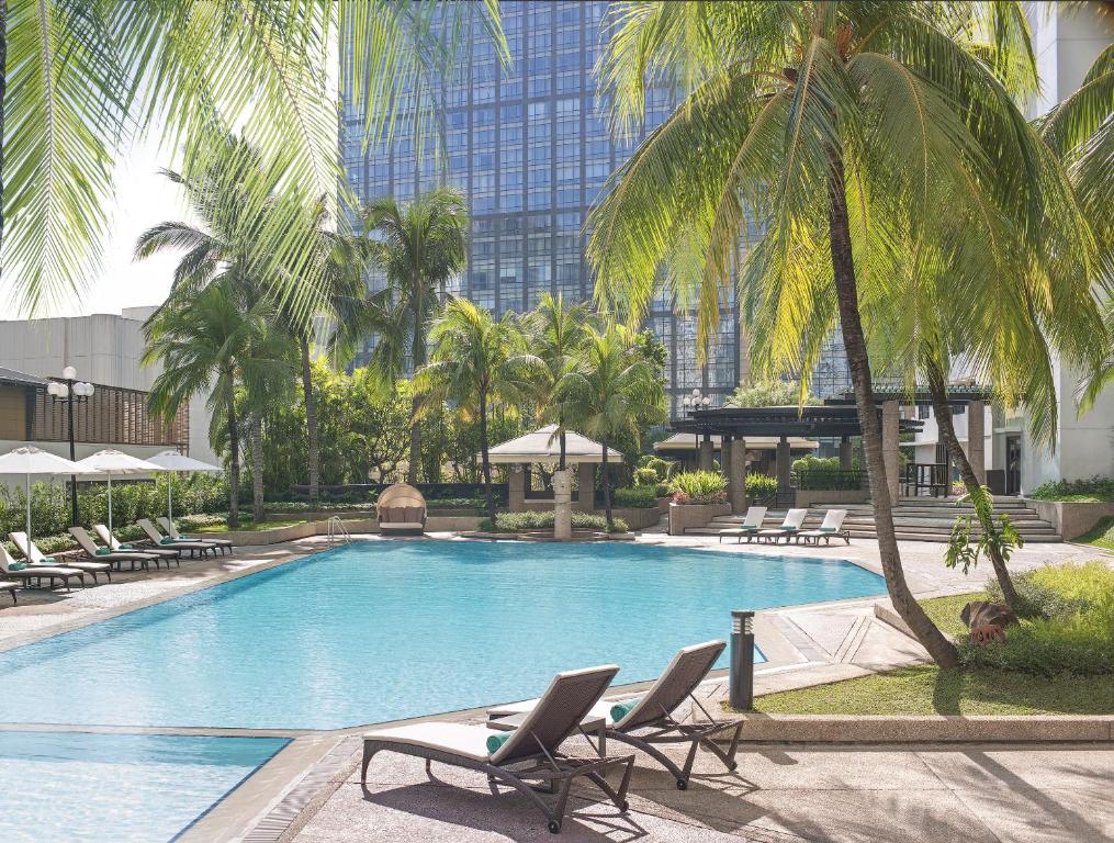 een zwembad met stoelen en palmbomen en een gebouw bij New World Makati Hotel, Manila in Manilla