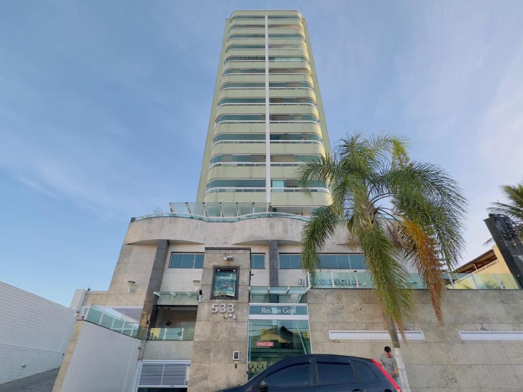 um edifício alto com uma palmeira em frente em Apartamento Cidade Ocian - Praia Grande - Edifício Van Gogh - Alto padrão 94mts - 2 Suítes na Praia Grande