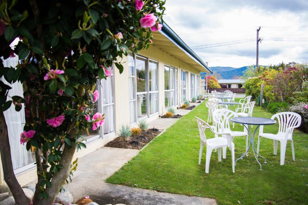 a patio with white chairs and tables and flowers at Alpenhorn Motel in Te Anau
