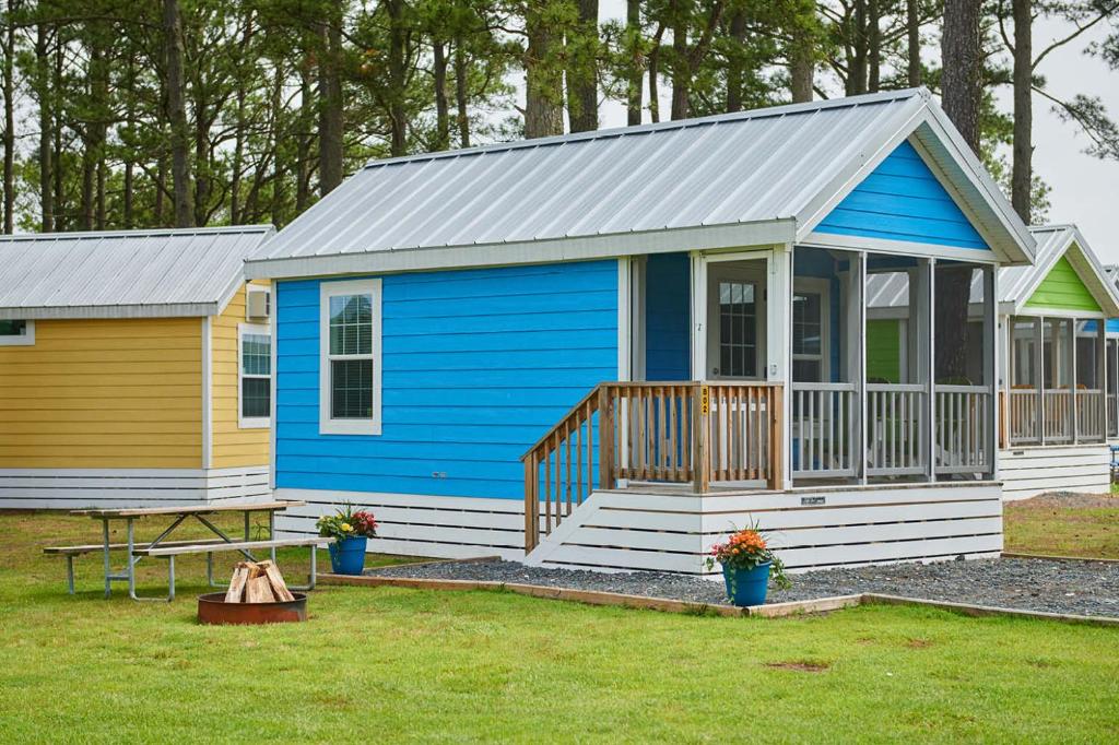 a blue and yellow tiny house with a porch at Jellystone Park Chincoteague Island in Chincoteague