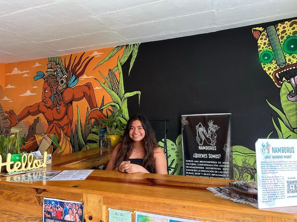 Eine Frau, die an einer Theke in einem Restaurant mit Wandgemälde sitzt. in der Unterkunft Hostal Namborus in Rivas