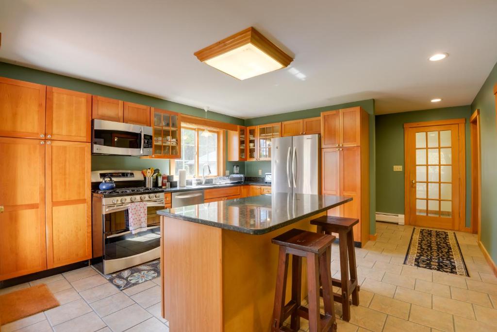 a kitchen with wooden cabinets and an island with bar stools at Charming Putney Home Porch, Grill and Hiking Trails in Putney