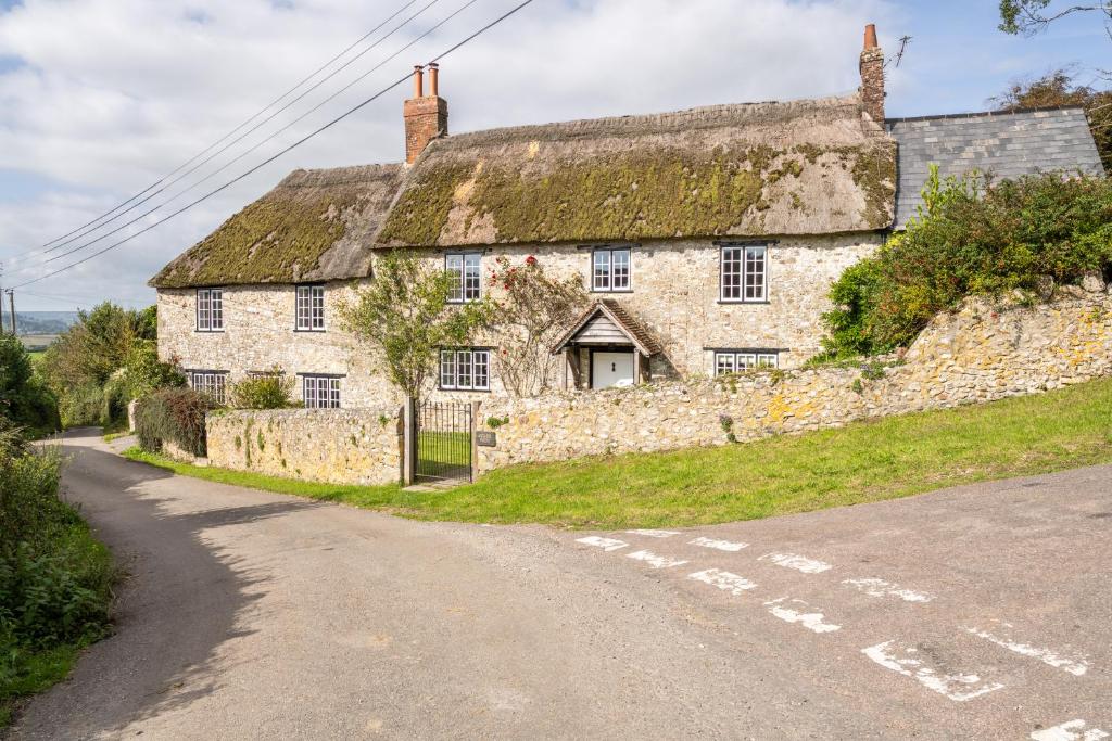 an old stone house with a grass roof on a road at Charming Family Farmhouse near Lyme Regis in Axminster