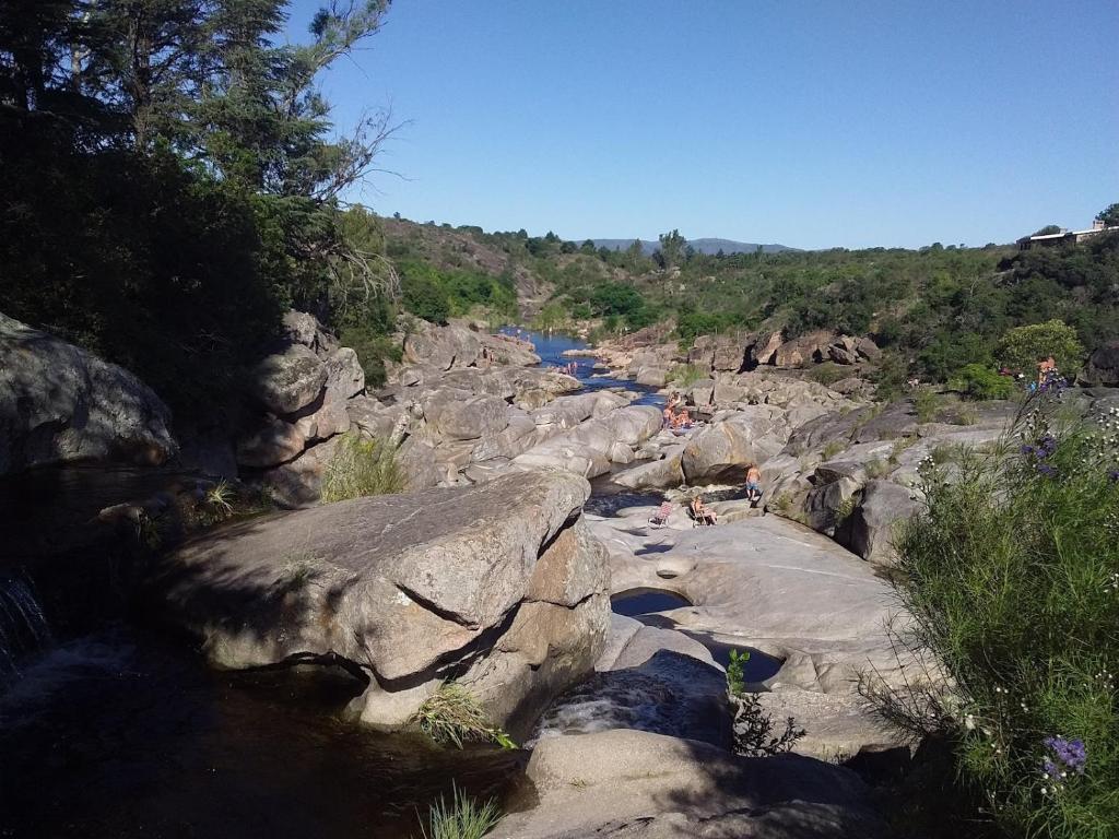 a river with people sitting on the rocks next to a mountain at La Allandesa in Cavalango
