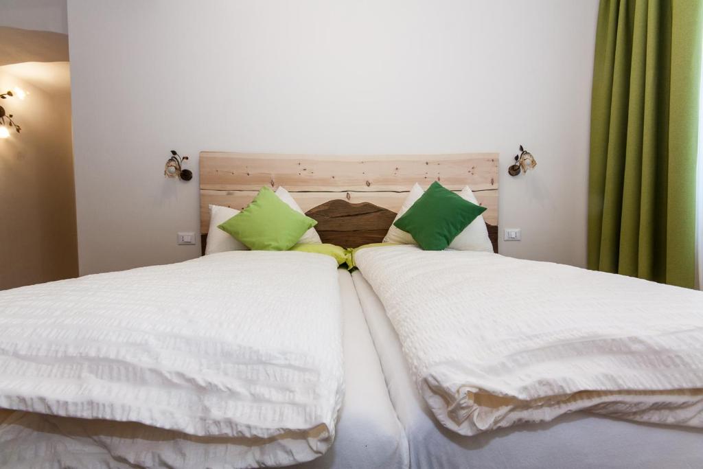 Duas camas com lençóis brancos e almofadas verdes em B&B Incanto em Cles
