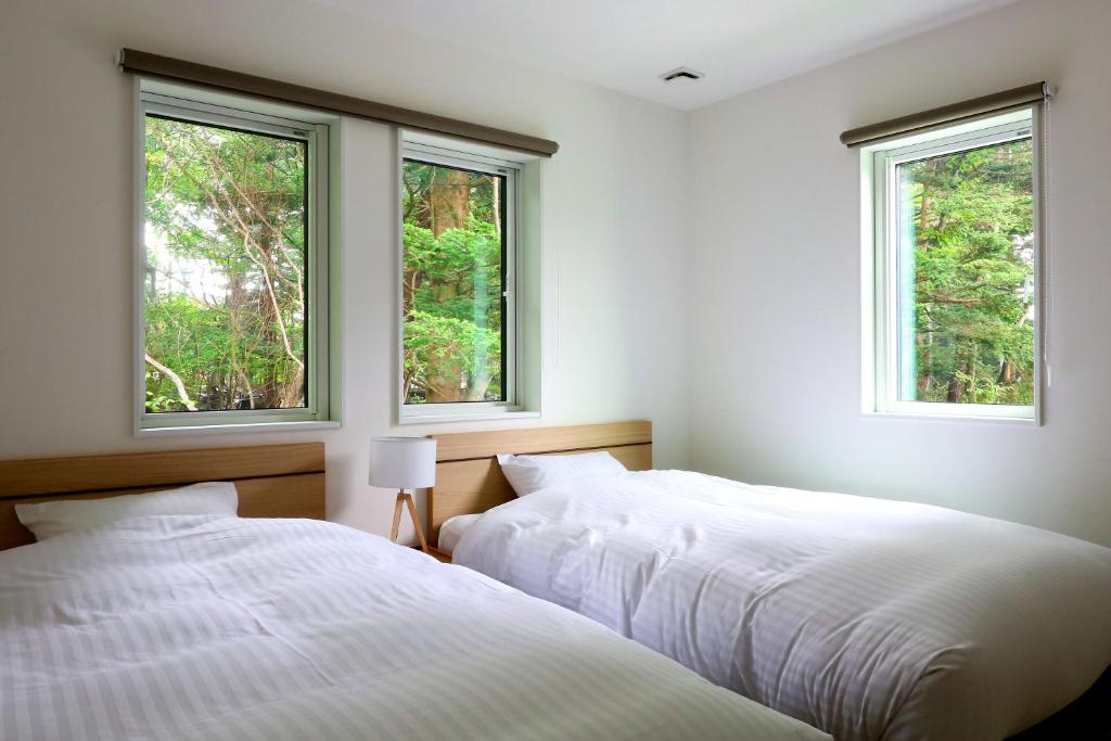 two beds in a bedroom with two windows at Albatross Karuizawa in Karuizawa