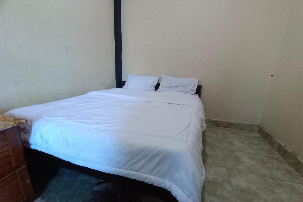 un letto con lenzuola e cuscini bianchi in una stanza di OYO 93207 Merah House a Pekanbaru