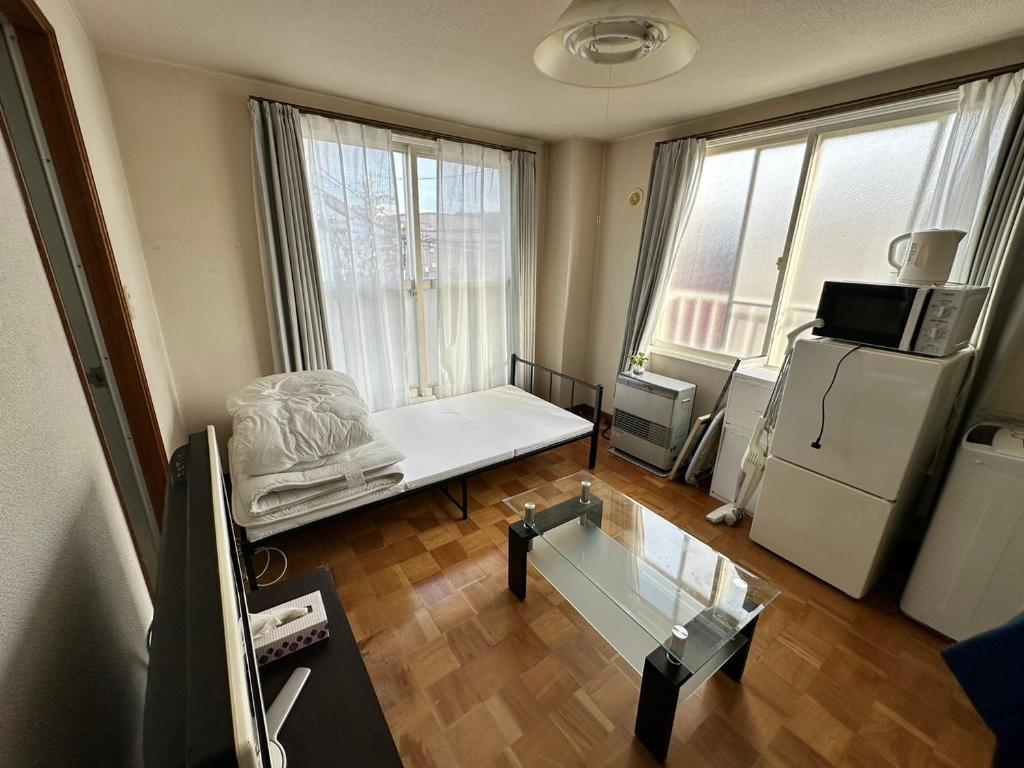 Toyohiraにあるカプリス豊平公園201号室のベッド1台、冷蔵庫が備わる小さな客室です。
