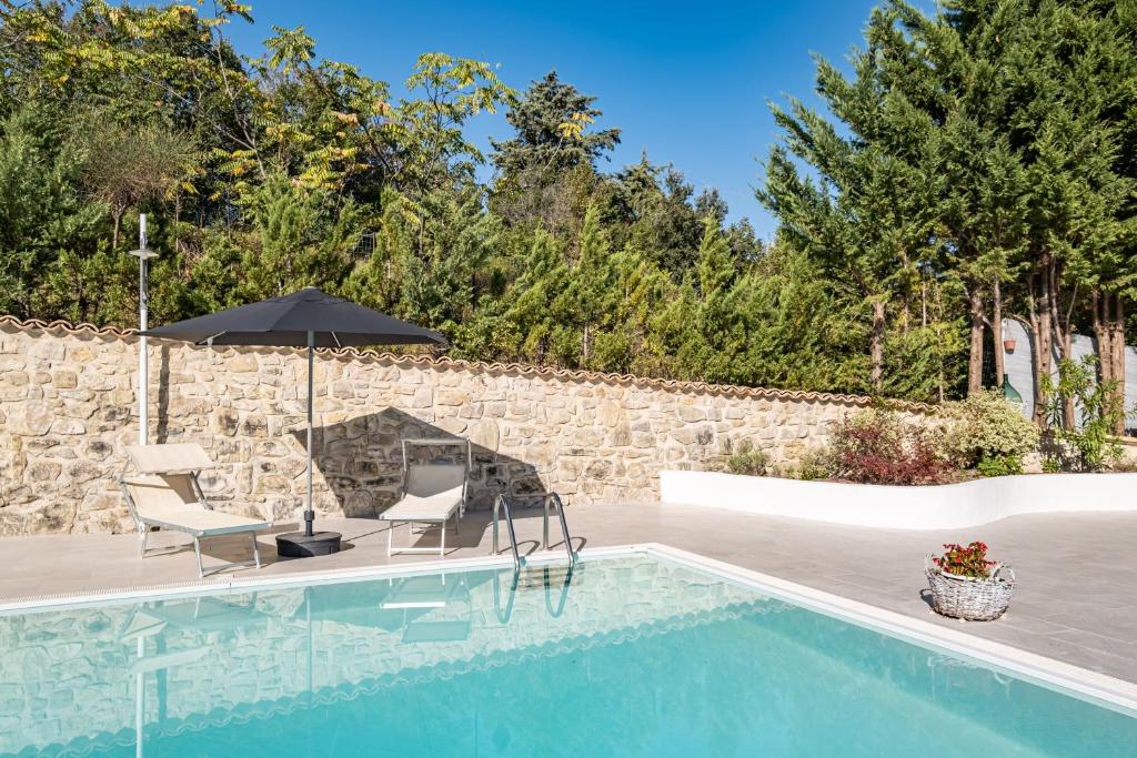 a pool with chairs and an umbrella next to a stone wall at Borgo Majella by Rentbeat in Abbateggio
