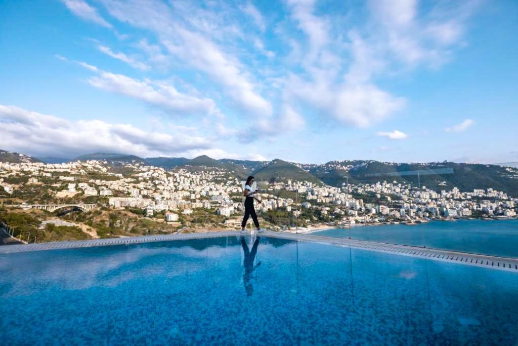 a man standing on the edge of a swimming pool overlooking a city at Monte Cassino in Jounieh
