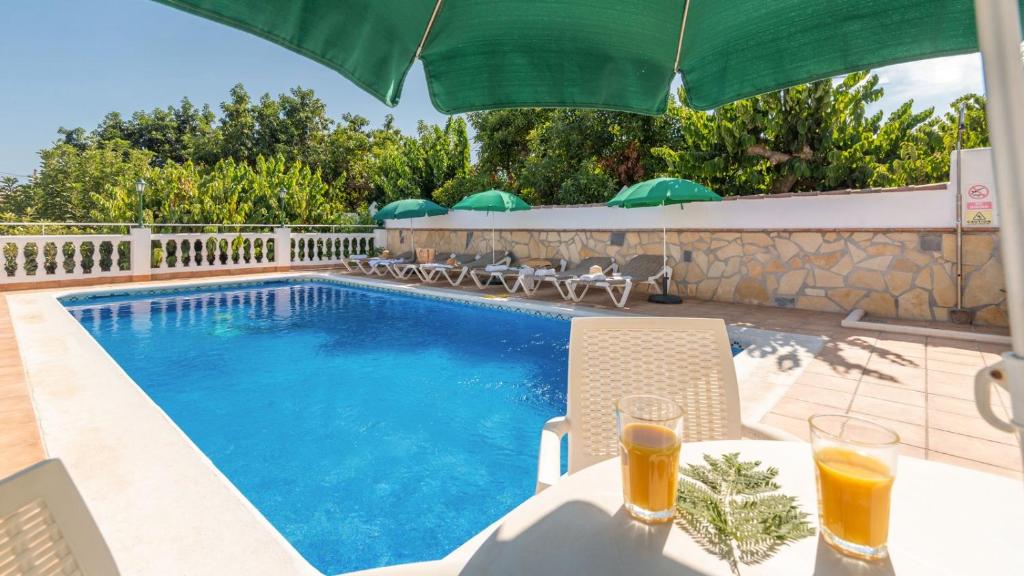 una piscina con mesa y 2 vasos de zumo de naranja en Villa Cañadu Nerja by Ruralidays, en Nerja