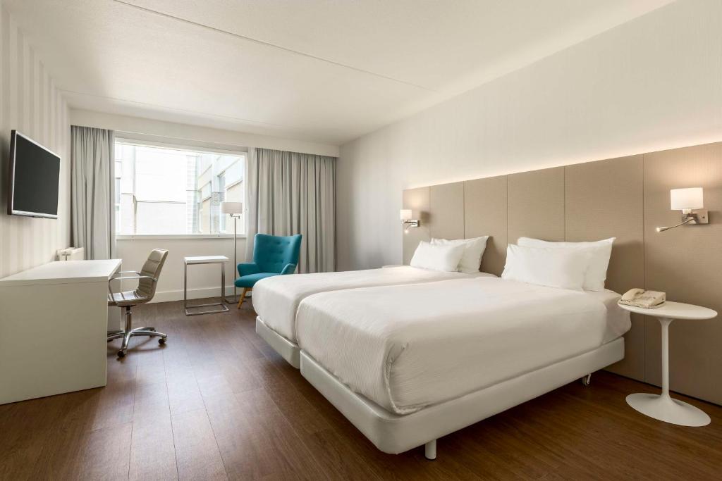 um quarto de hotel com uma grande cama branca e uma secretária em NH Amsterdam Schiphol Airport em Hoofddorp