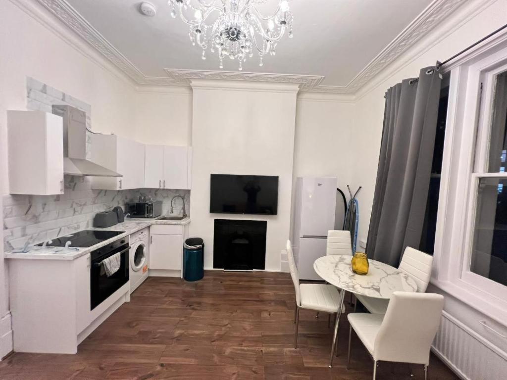 a white kitchen with a table and chairs and a chandelier at Iconic One Bed Apartment in Chiswick in London