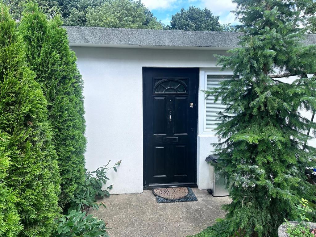 una puerta negra en una casa blanca con un árbol en Self-contained Annex for short stay, en Bushey