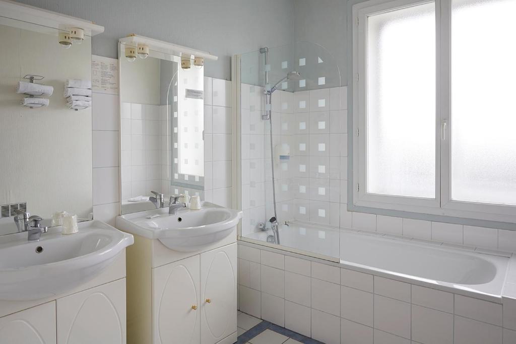 a white bathroom with two sinks and a tub and a window at The Originals City, Hôtel Les Océanes, Lorient in Lorient