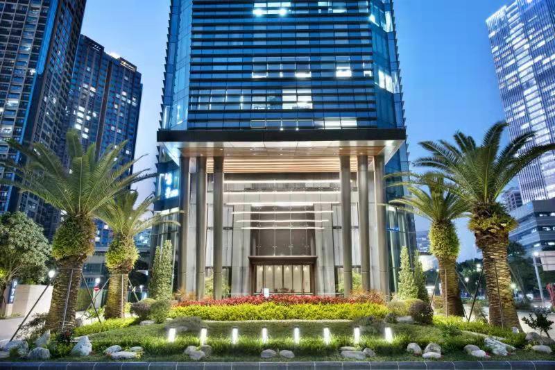 a large building with palm trees in front of it at Hamps Hotel ShenZhen in Shenzhen