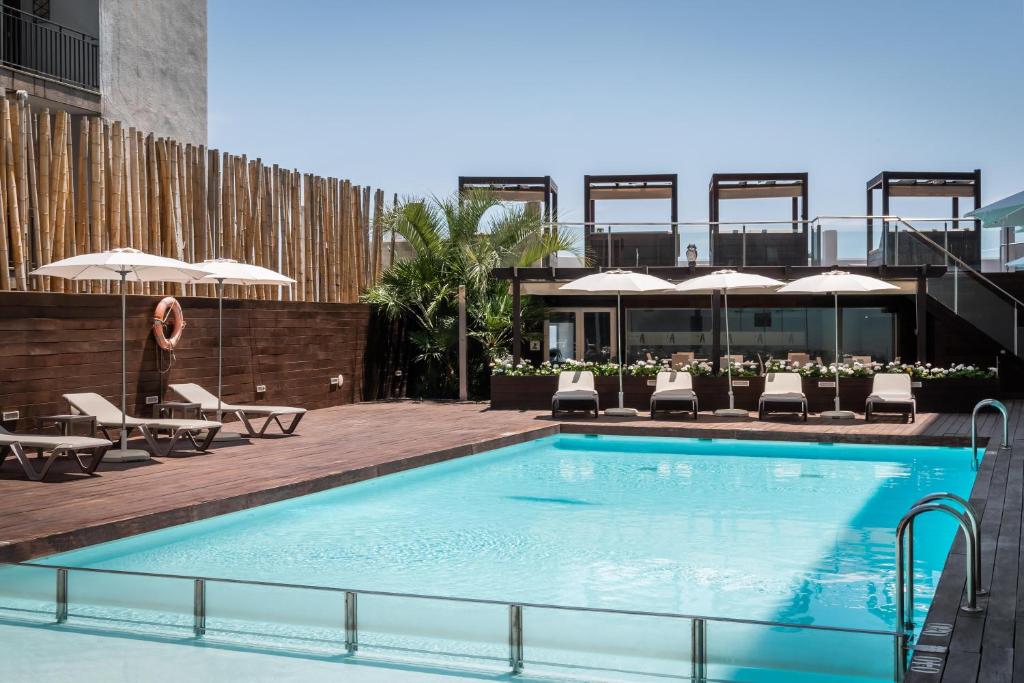 una piscina con sillas y sombrillas en un edificio en ALEGRIA Sun Village en Lloret de Mar