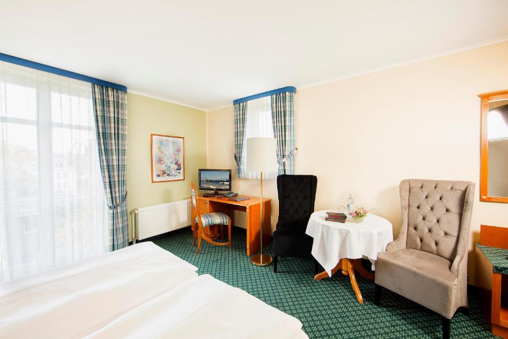 グライフスヴァルトにあるHotel Kronprinzのベッド、デスク、椅子が備わるホテルルームです。