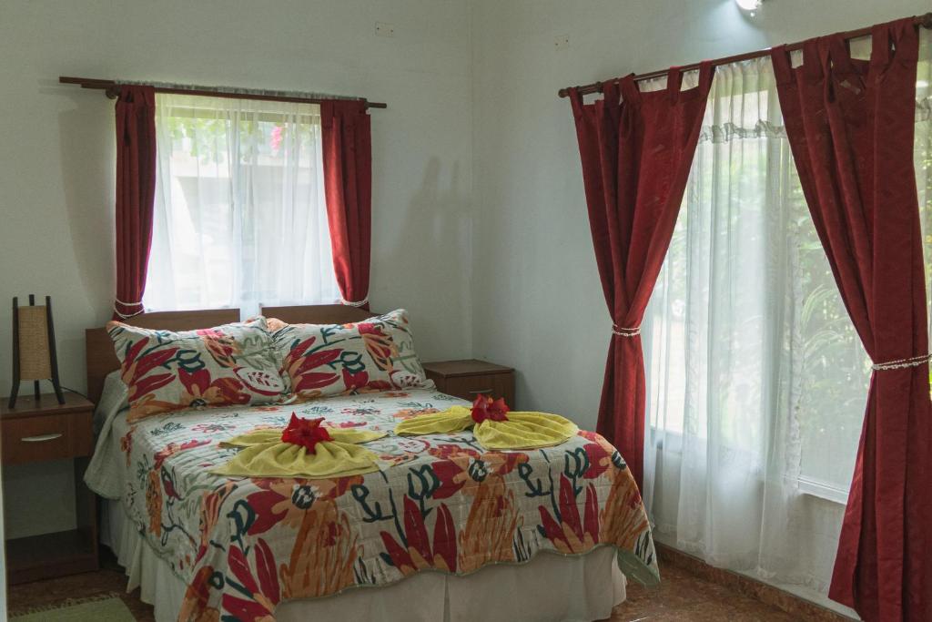 1 Schlafzimmer mit einem Bett und 2 Fenster mit roten Vorhängen in der Unterkunft Hostal y Cabañas Aorangi in Hanga Roa
