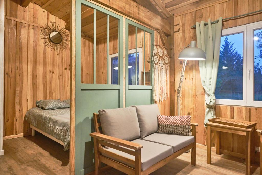Cette chambre dispose d'un canapé, d'un lit et d'une fenêtre. dans l'établissement Cabane de charme en pleine forêt - Domaine Temali, à Labouheyre