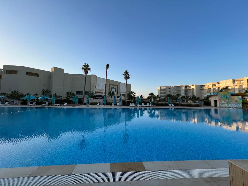 a large blue swimming pool with palm trees and buildings at Palm Lake Resort Folla Monastir/Sousse in Monastir