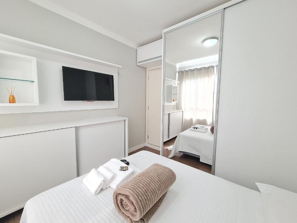 Habitación blanca con cama y espejo en Residencial Praia Brava Blue - Apartamentos, en Balneário Camboriú