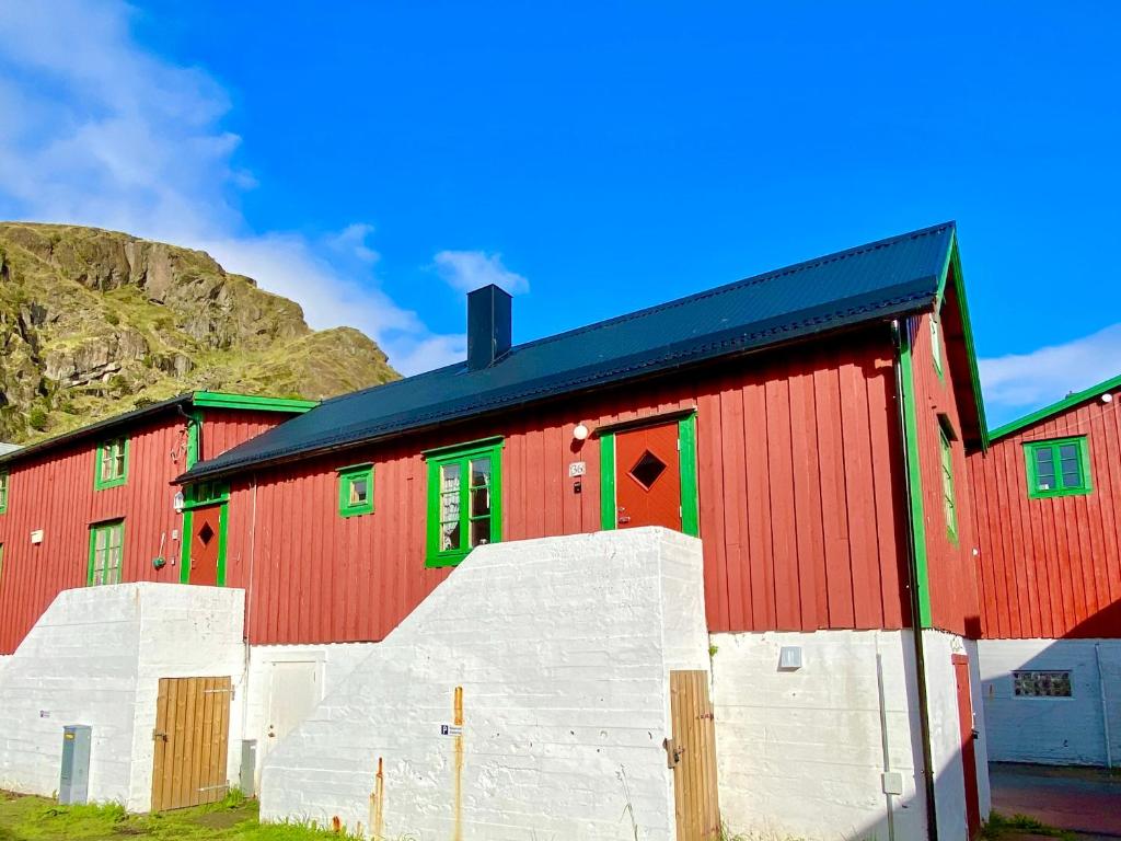 a red barn with green windows and a mountain at Charming Rorbu Stamsund Lofoten in Stamsund