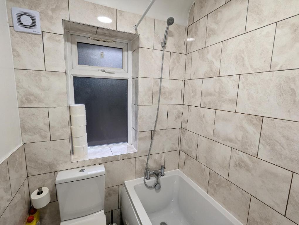 ein Bad mit einer Badewanne, einem WC und einem Fenster in der Unterkunft Fantastic 3-Bedroom House in London in Morden