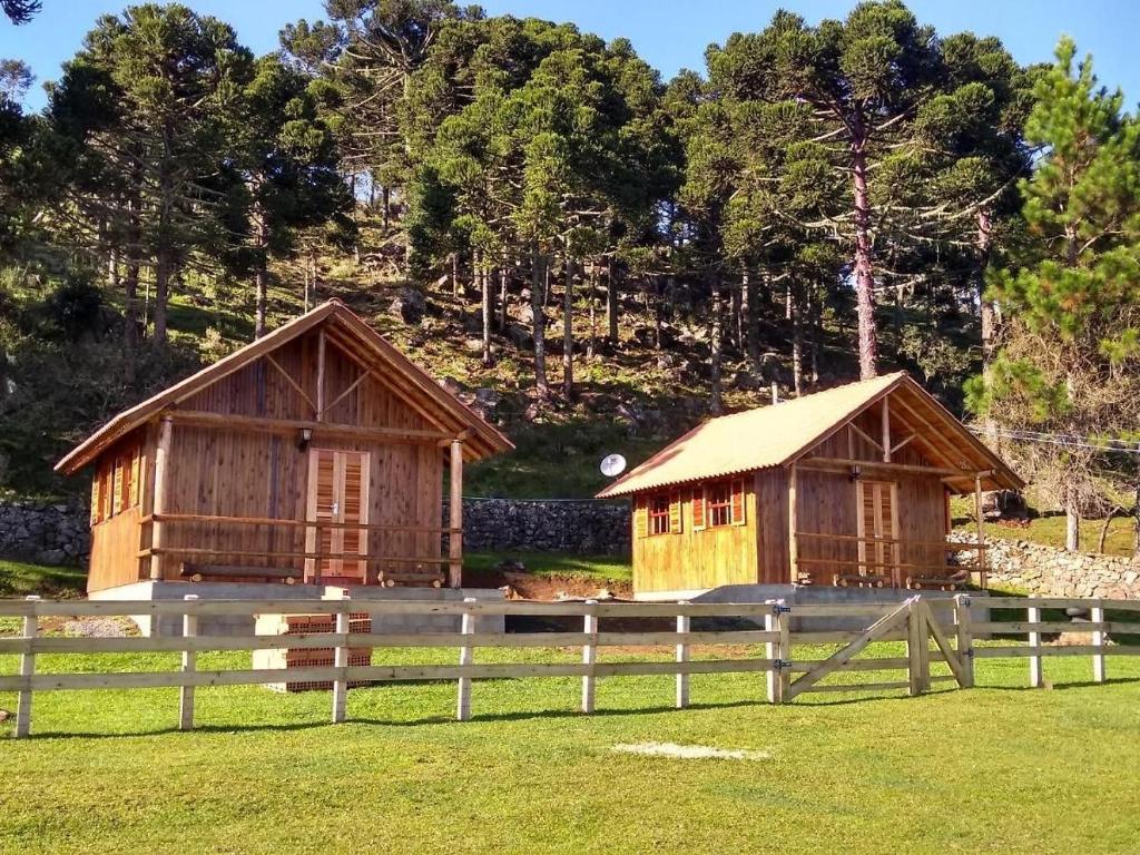 dois pequenos edifícios de madeira num campo ao lado de uma cerca em Pousada Laranjeiras Ecoturismo em Bom Jardim da Serra