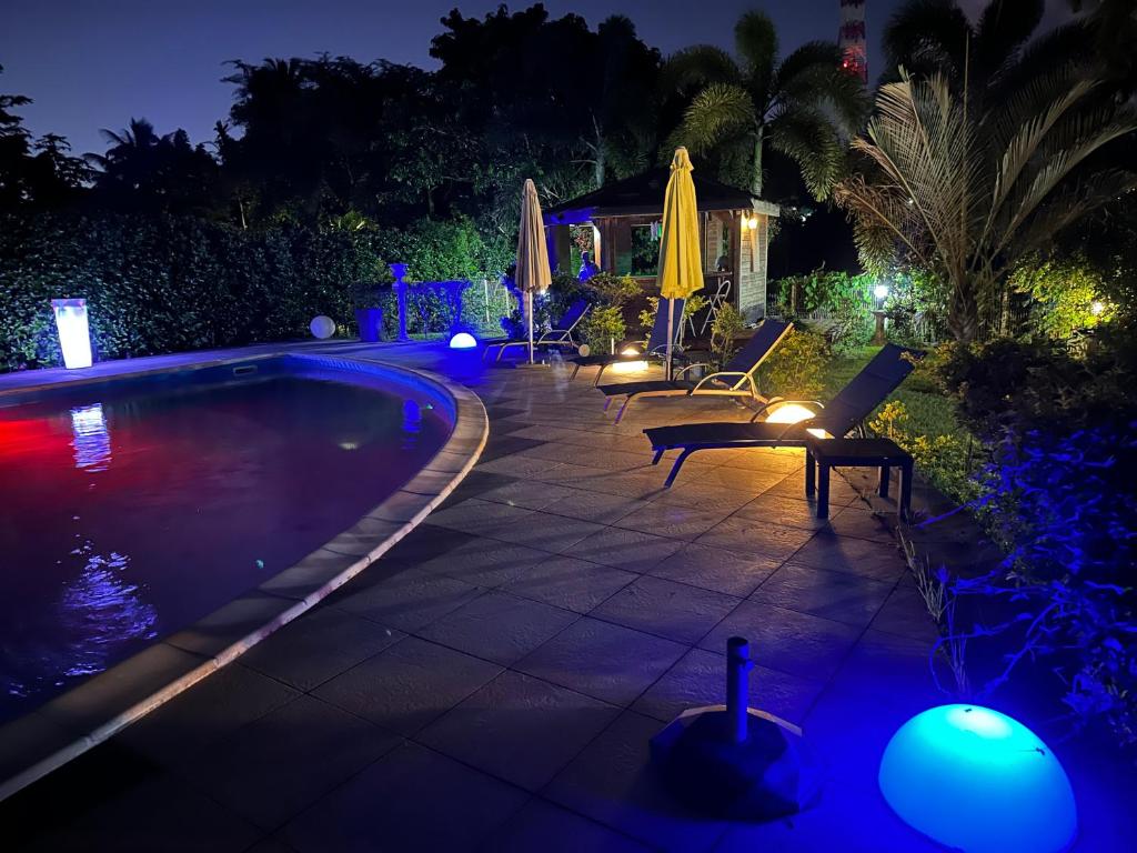 a swimming pool with chairs and umbrellas at night at Appartement Coeur de Papillon in Baie-Mahault